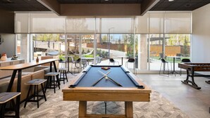 A pool table in a room with large windows, bar stools, and a casual seating area.
