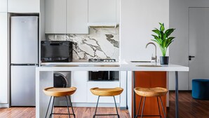 A modern kitchen with a marble backsplash, a built-in oven, and a stainless steel refrigerator. There are three wooden stools and a potted plant on the counter. - Boulevard 115 (Tashkent)