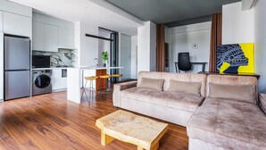 A modern living room with a beige sofa, a wooden coffee table, and a kitchen area with a washing machine. - Boulevard 115 (Tashkent)