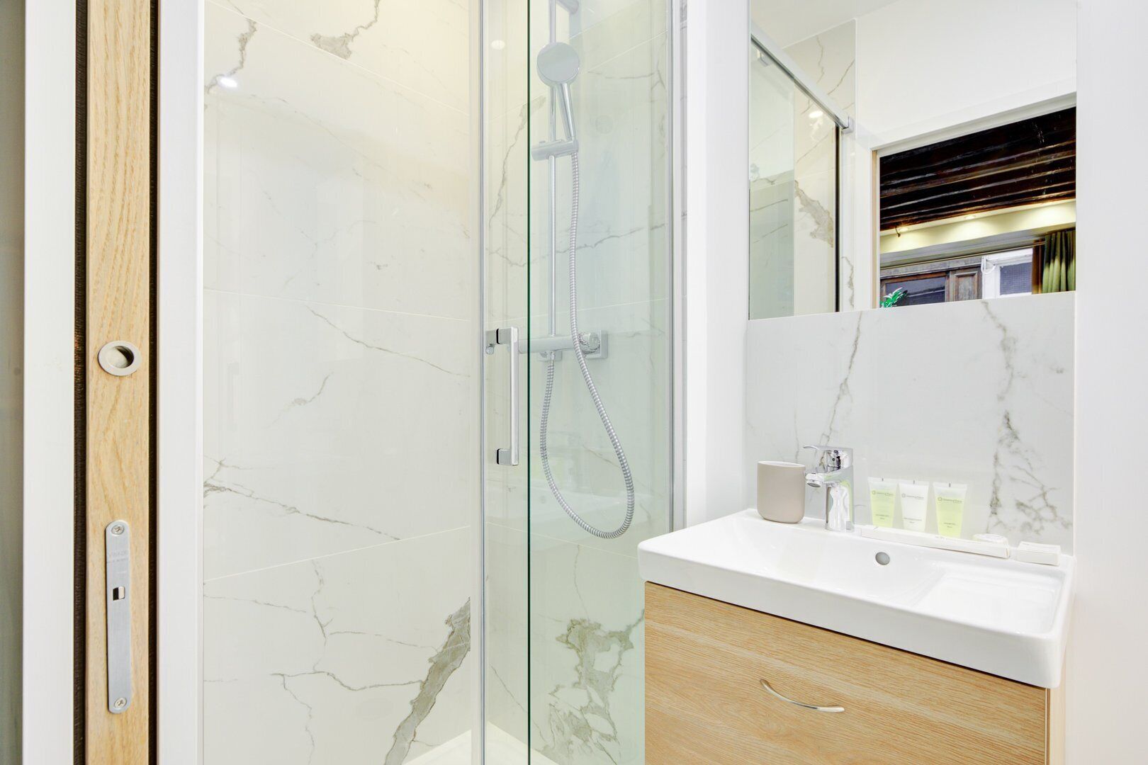 A modern bathroom with a glass-enclosed shower, a white marble sink, and a wooden vanity.