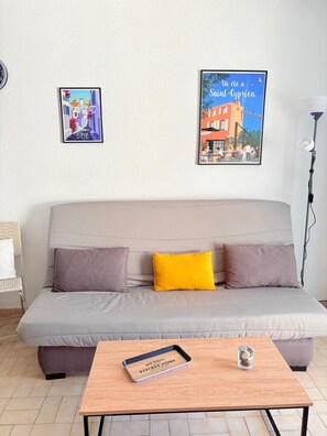 Ein Wohnzimmer mit einer Couch, zwei Kissen, einem Couchtisch mit Tablett und zwei gerahmten Bildern an der Wand.