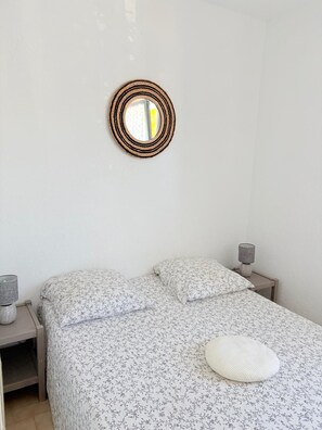 Ein Schlafzimmer mit einem Bett, einer Nachttischlampe, einem Wandspiegel und einem Nachttisch.