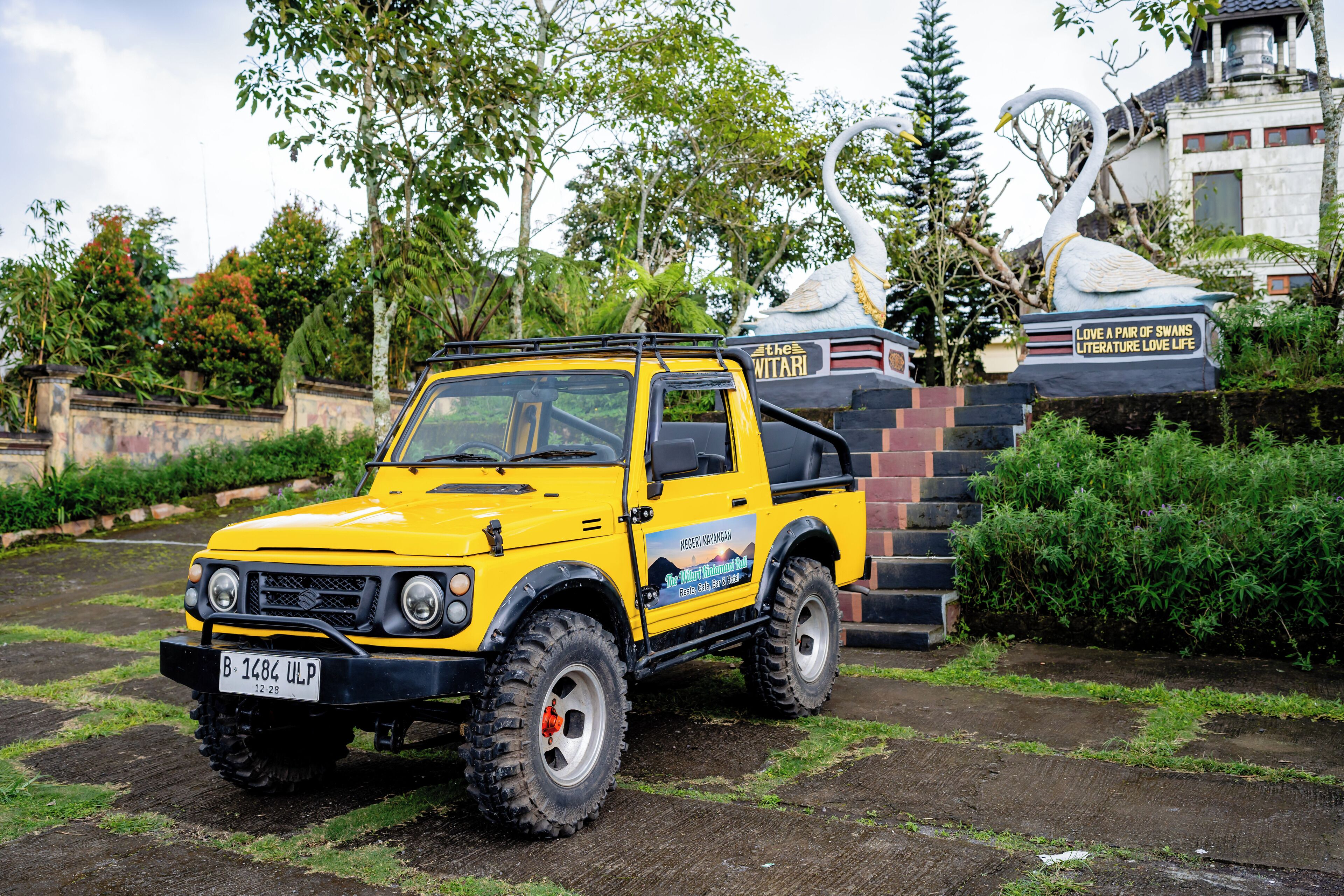 A yellow off-road vehicle parked in a garden with a swan statue and a sign that reads "Love a pair of swans literature love life".