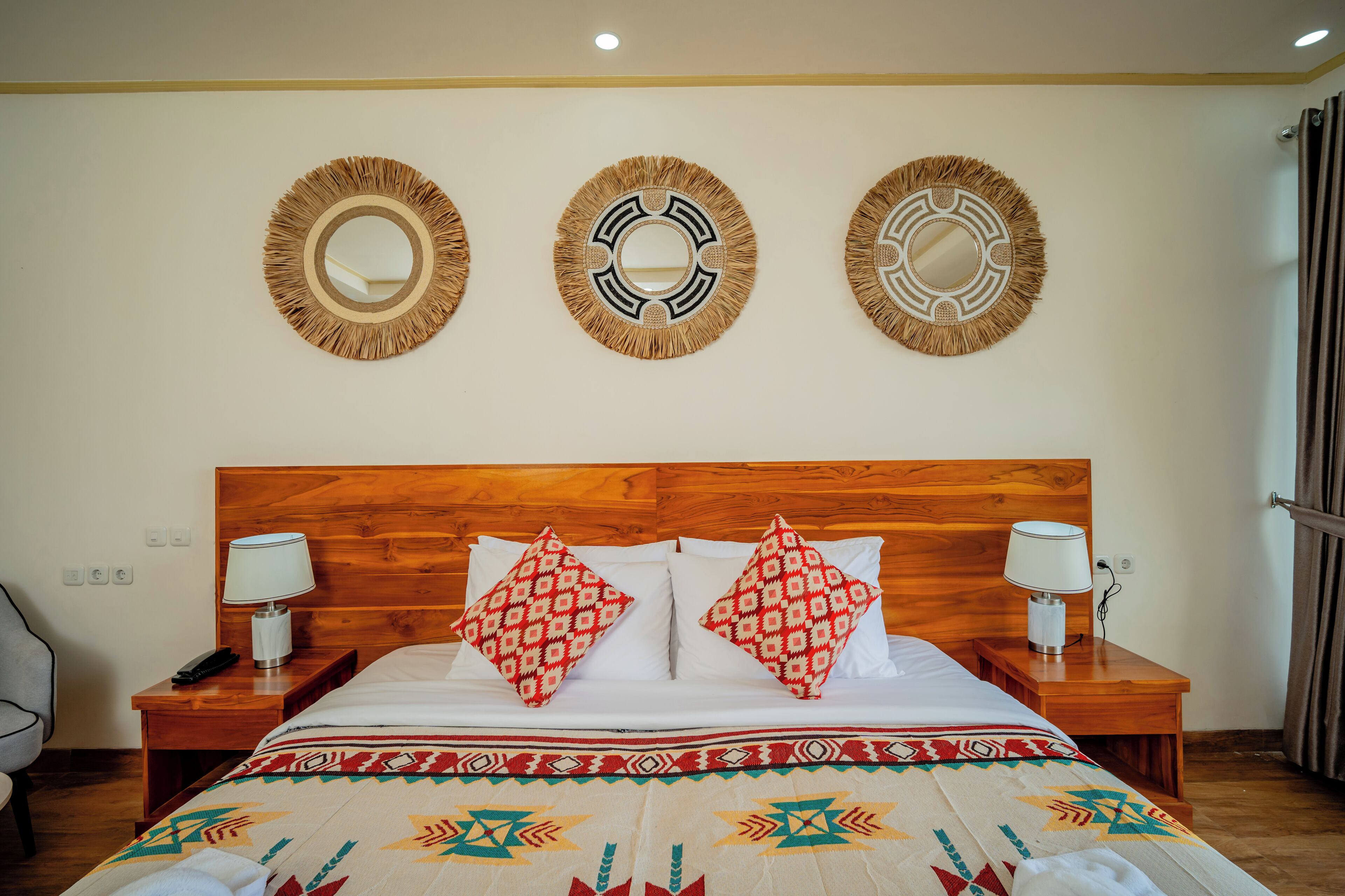 A hotel room with a wooden headboard, a bed with patterned pillows, bedside lamps, and three wall-mounted mirrors.