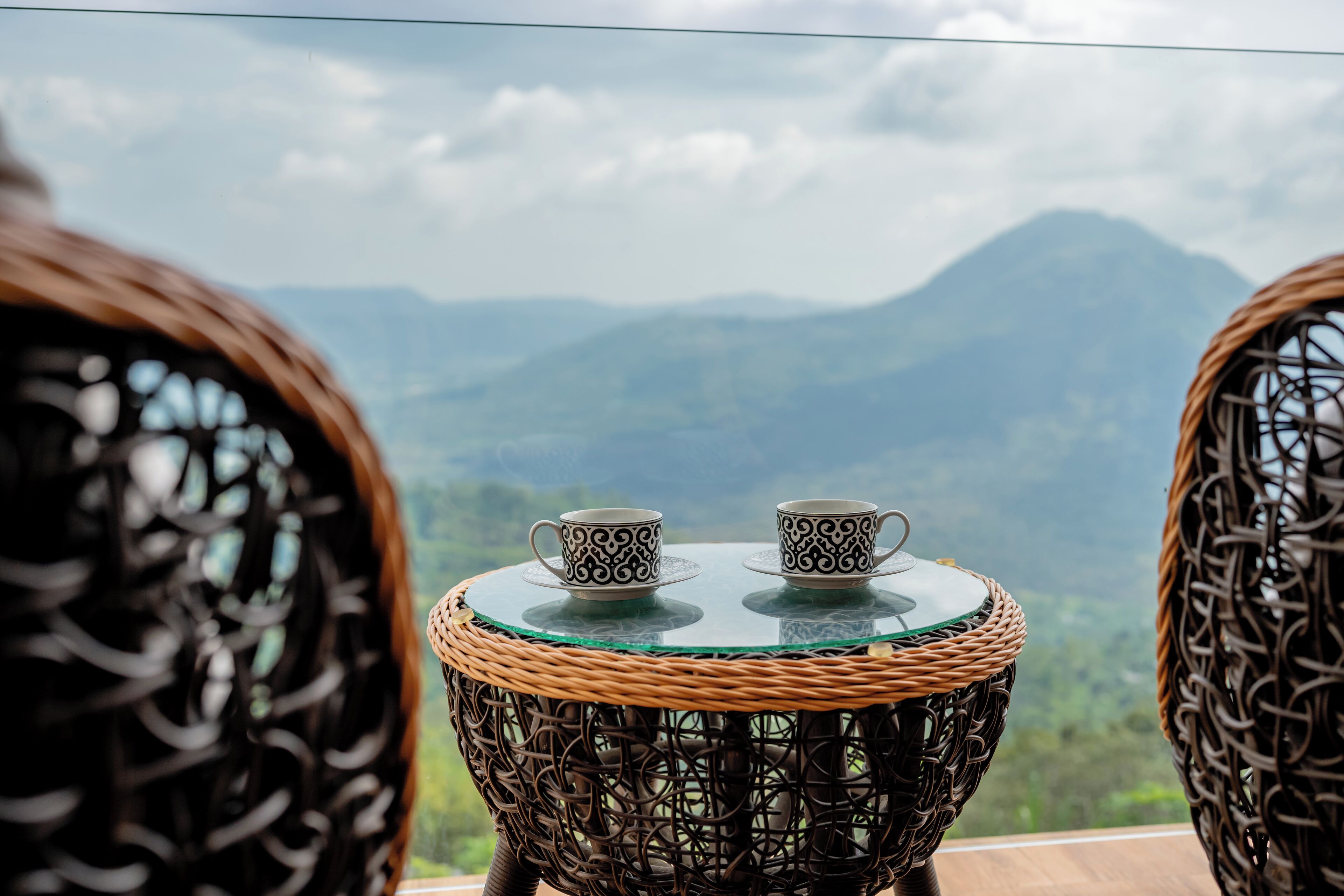 A wicker table with two cups and saucers, overlooking a mountainous landscape.