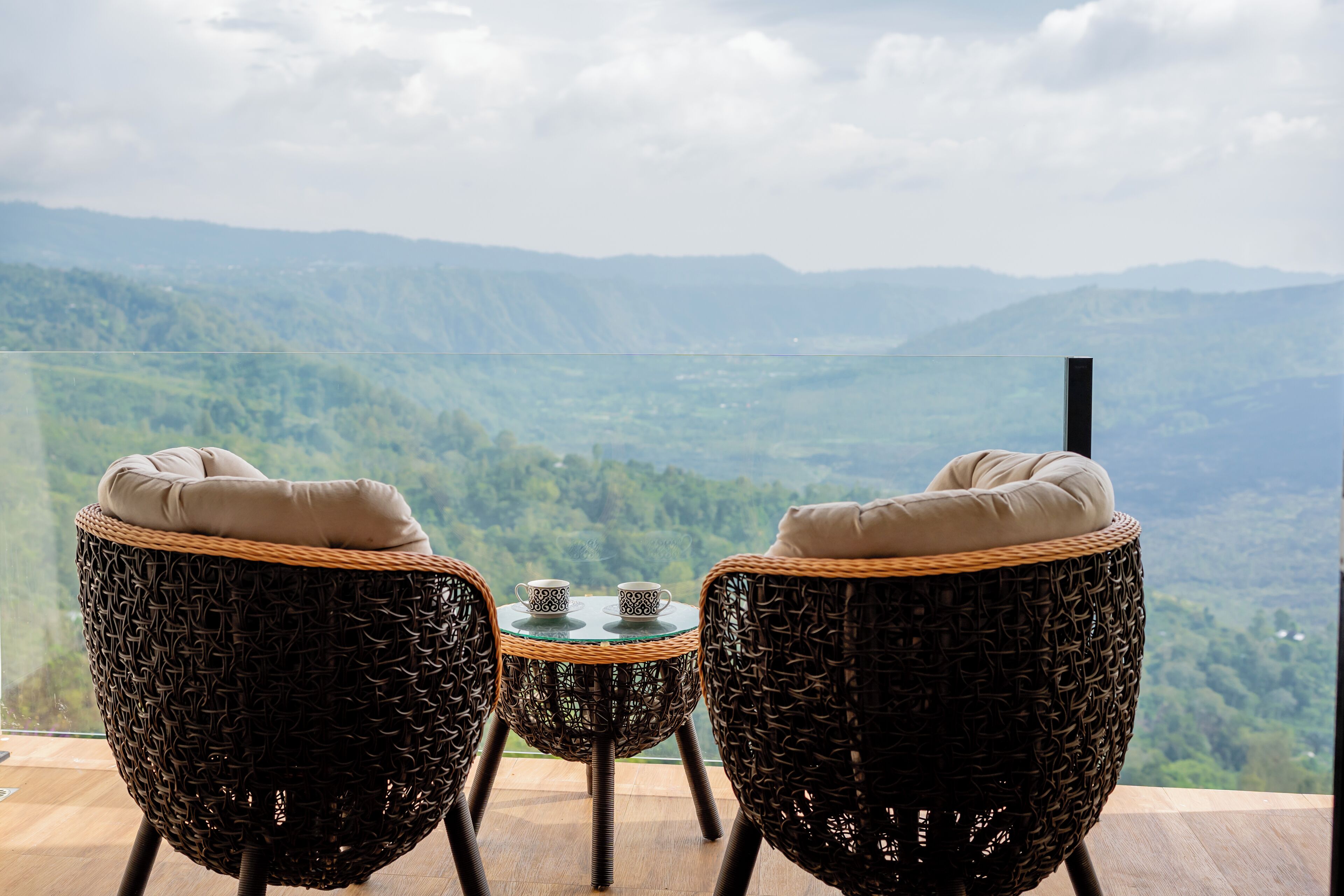 Un balcón con sillones de mimbre y una pequeña mesa, con vistas a un paisaje montañoso.