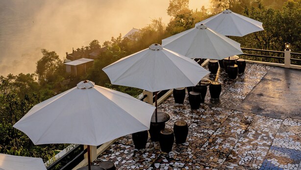 Une terrasse agrémentée de parasols et de plantes en pot, offrant une vue sur un plan d’eau et des montagnes.