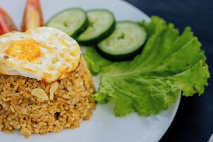 Un plato de arroz frito coronado con un huevo frito, acompañado de rodajas de pepino y lechuga.