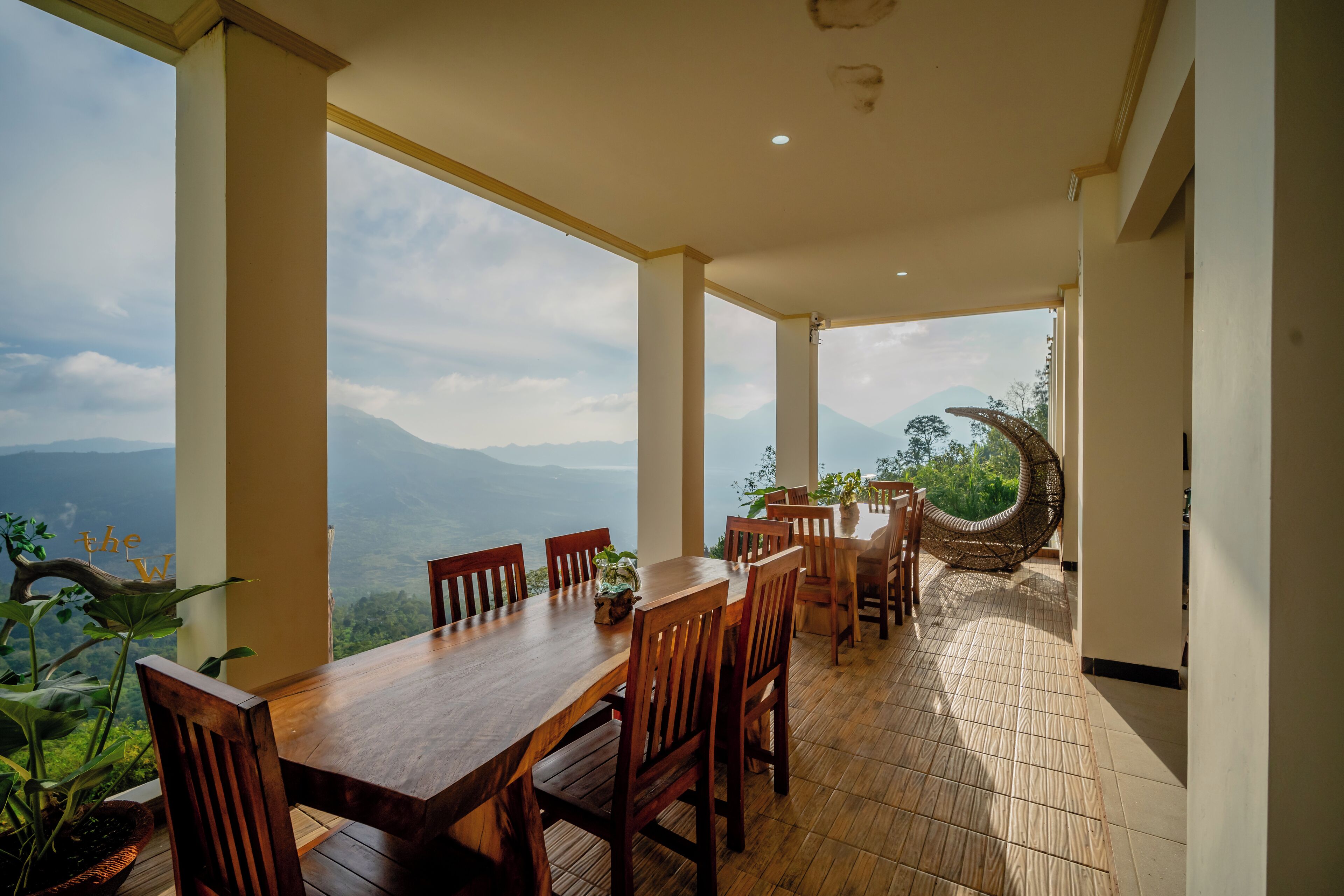 A dining area with a wooden table and chairs, large windows offering a view of mountains, and a hanging chair.