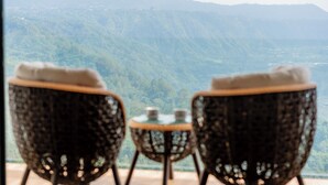Une vue depuis un balcon, avec des fauteuils en osier et une petite table, donnant sur un paysage montagneux.