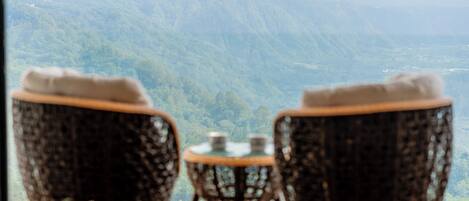 Une vue depuis un balcon, avec des fauteuils en osier et une petite table, donnant sur un paysage montagneux.
