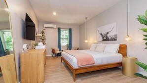 A bedroom with a bed, a desk, a chair, a TV, and a window. - Hydrangea Deluxe King Studio at The Dogwood (Maggie Valley)