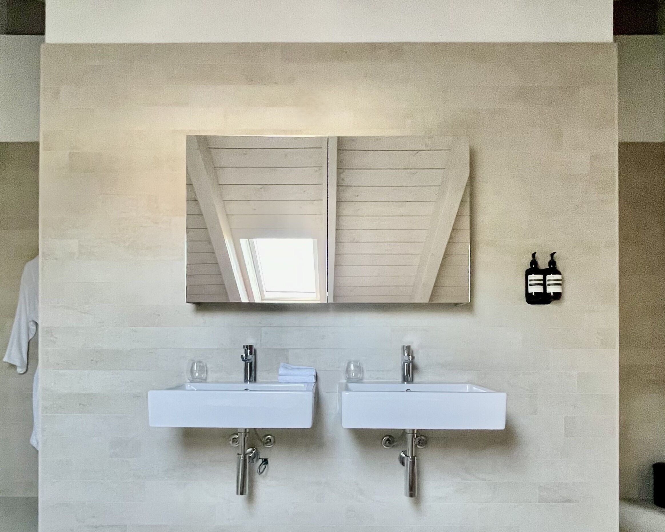 Un baño con dos lavamanos, un espejo grande y un perchero para toallas.