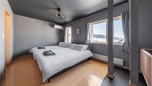 Une chambre moderne avec un grand lit, un ventilateur de plafond et une vue sur l’extérieur grâce à de grandes fenêtres.