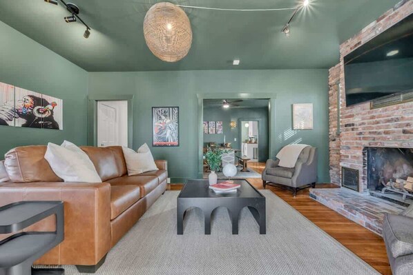A living room with a brown leather sofa, a black coffee table, and a brick fireplace.