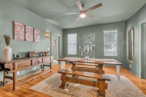 Enjoy meals at the large dining table surrounded by benches in this room with a high ceiling and ceiling fan.