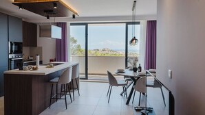 A modern kitchen with a central island, dining area with chairs, and a large window offering a view of the city. - A bright and cozy Mellieha apartment with modern comforts, close to the beach, shops, and transport—perfect for a relaxing family or couple’s getaway. (Il-Mellieħa)