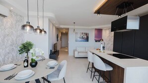 A modern kitchen with a dining area, featuring pendant lights, a central island, and a black cabinetry. - A bright and cozy Mellieha apartment with modern comforts, close to the beach, shops, and transport—perfect for a relaxing family or couple’s getaway. (Il-Mellieħa)