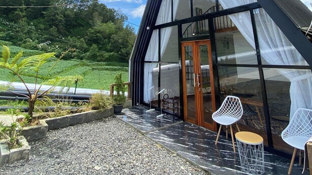 Ein modernes Gebäude mit großen Glasfenstern und einem geneigten Dach, umgeben von einer Schotterterrasse mit Sitzgelegenheiten.