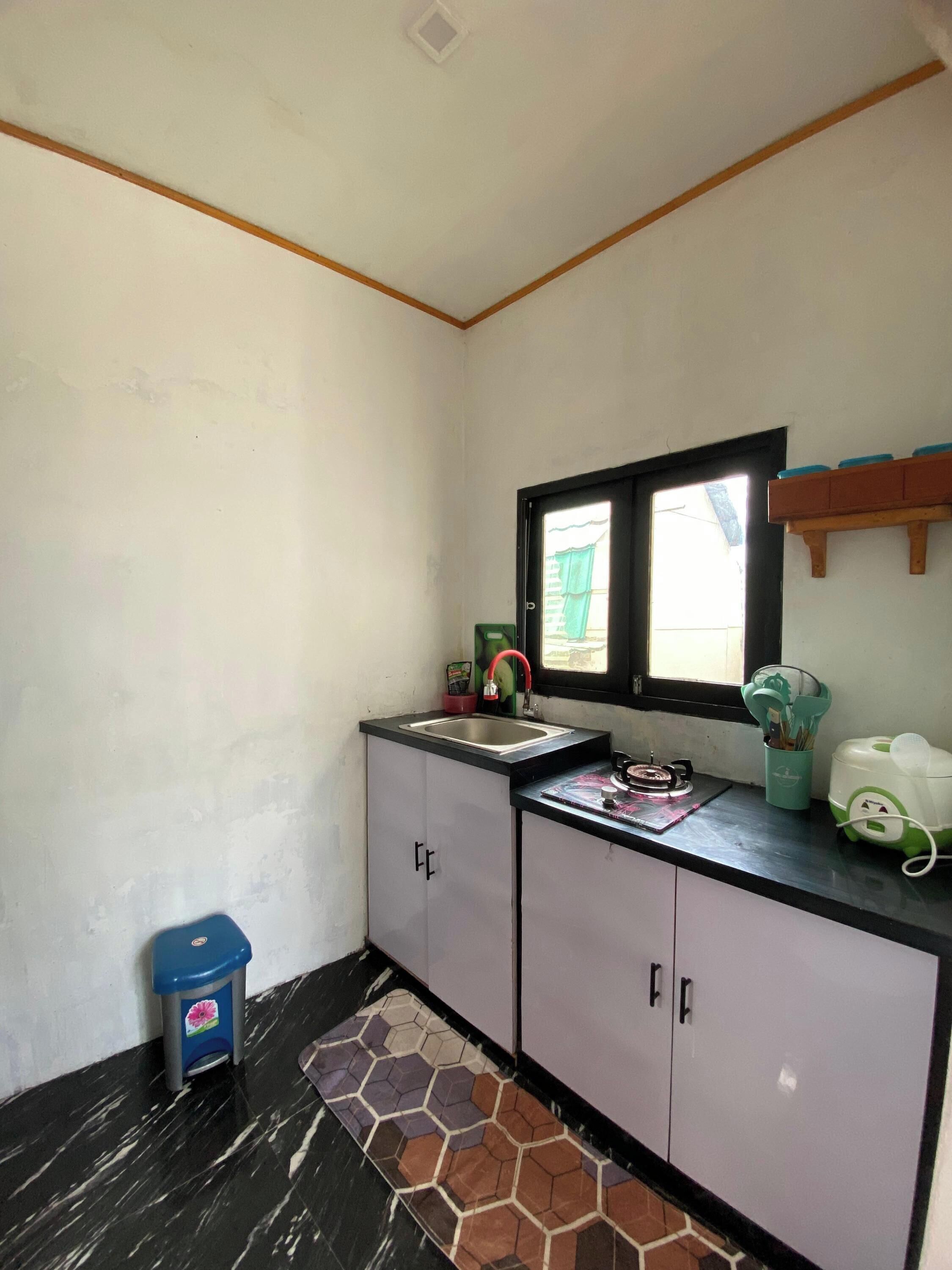 A small kitchen with a sink, a window, and a trash bin.