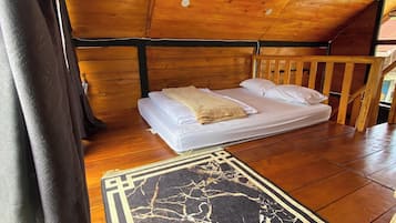 Una stanza accogliente con soffitto in legno, un letto con lenzuola bianche e un tappeto decorato con motivi neri e dorati.