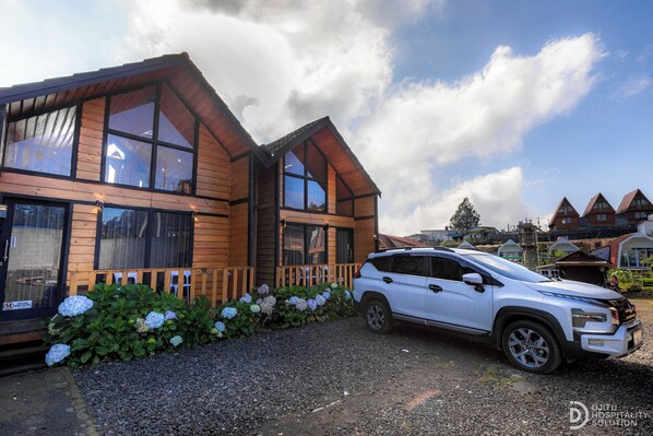 A wooden cabin with large windows, a gravel driveway, and a white SUV parked in front. - Zaa Villa (Dieng Kulon)