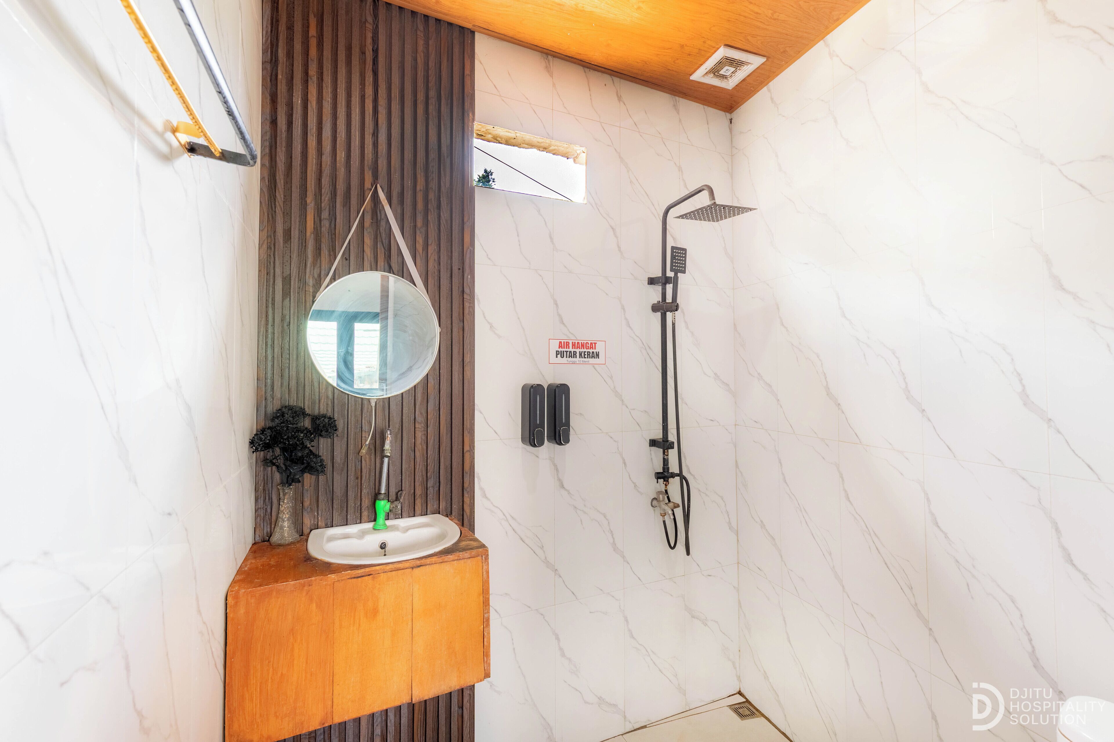 A bathroom with a wooden vanity, a sink, a mirror, a shower, and a marble wall.