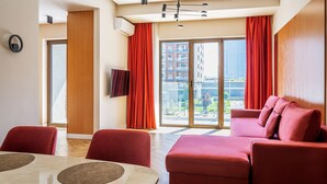 Une chambre d’hôtel moderne dotée d’une grande porte-fenêtre coulissante donnant sur l’extérieur, d’un canapé rouge, d’une table à manger avec des chaises et d’un téléviseur à écran plat fixé au mur.