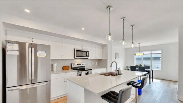 A modern kitchen with stainless steel appliances, a central island with bar stools, and pendant lighting. - Beautiful 3 bedroom home in Glenridding ravine  (Edmonton)