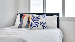 A bed with white bedding and multiple pillows, including a decorative one with blue patterns, in a room with a window. - Beautiful 3 bedroom home in Glenridding ravine  (Edmonton)