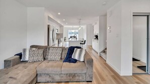 A modern living room with a sofa, a dining area, and a kitchen in the background. - Beautiful 3 bedroom home in Glenridding ravine  (Edmonton)