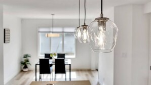 A modern dining area with pendant lights, a dining table, chairs, and a window with blinds. - Beautiful 3 bedroom home in Glenridding ravine  (Edmonton)