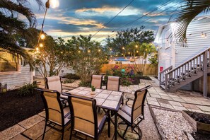 Pátio com mesa e cadeiras, cercado por plantas e um deck de madeira.