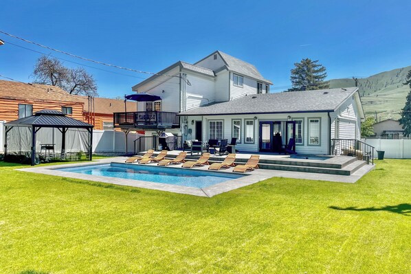 Una casa de dos pisos con piscina, un porche cubierto y un patio trasero cercado.
