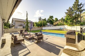 Un patio trasero con piscina, mobiliario exterior y una parrilla.