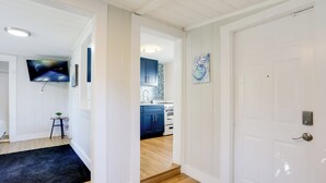 A hallway leading to a kitchen with white walls, a black rug, and a TV mounted on the wall. - 1 Mi to Lake Worth Beach Park: Chic Studio (Lake Worth Beach)