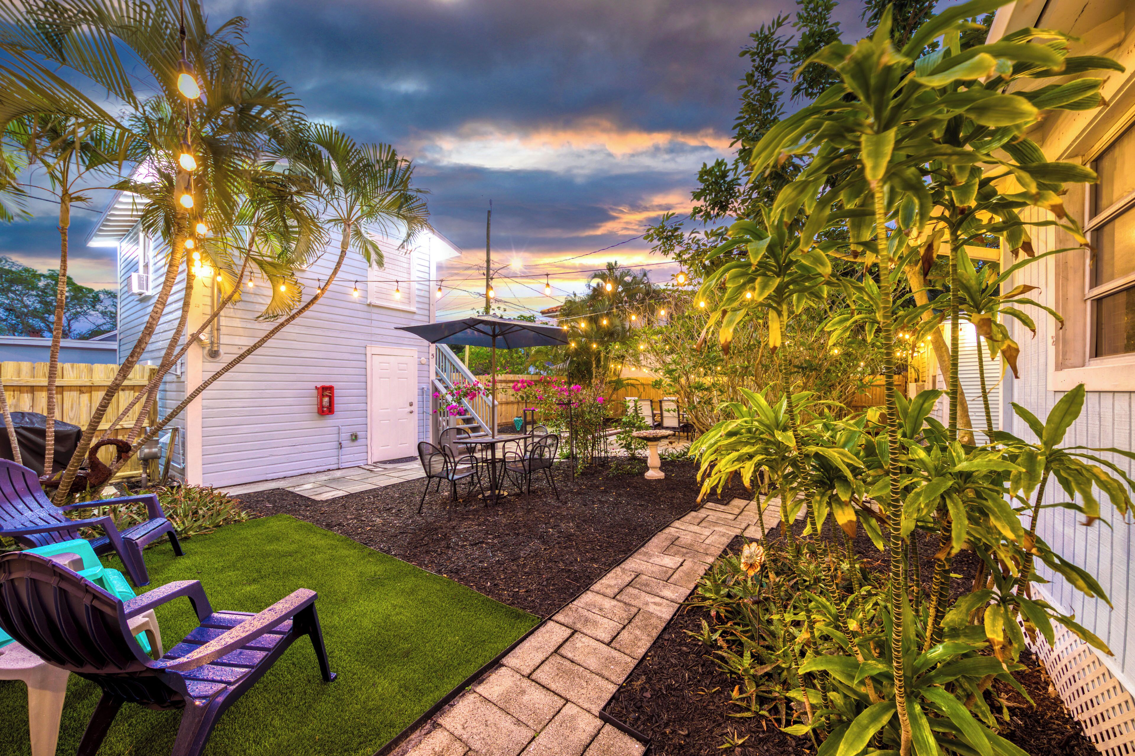 A backyard with artificial grass, a patio with chairs, a small table, and a wooden fence.
