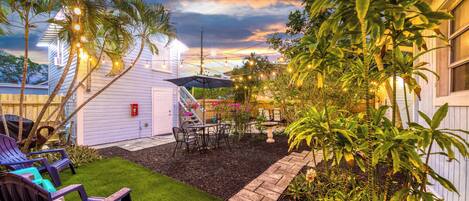 A backyard with artificial grass, a patio with chairs, a small table, and a wooden fence.