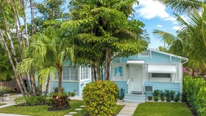 A light blue house with a white door, surrounded by lush greenery and palm trees. - 1 Mi to Lake Worth Beach Park: Chic Studio (Lake Worth Beach)