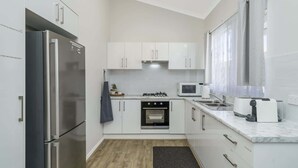 Een kleine keuken met witte kasten, een roestvrijstalen koelkast, een magnetron, een fornuis en een spoelbak.