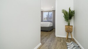Een smalle gang die leidt naar een slaapkamer met een bed, een bloempot en een paar slippers op de vloer.