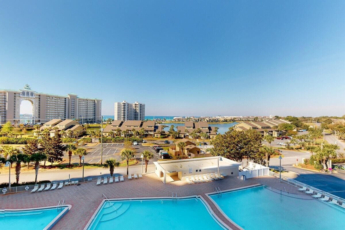 A resort with multiple swimming pools, a large building with an arched entrance, and a view of the sea.