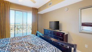 A hotel room with a bed, a TV on a dresser, a balcony with curtains, and a view of the city. - Gulf Views | Resort | Pools | Gulf View Getaway | Pickleball | Miramar Beach (Destin)
