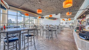 A spacious dining area with high ceilings, hanging orange pendant lights, and large windows offering views of the cityscape. - Gulf Views | Resort | Pools | Gulf View Getaway | Pickleball | Miramar Beach (Destin)
