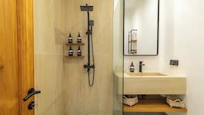 A modern bathroom with a wooden door, a glass shower enclosure, a beige tiled wall, a wooden vanity with a sink, and a mirror.