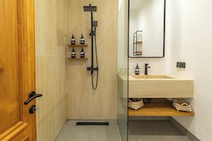 Een moderne badkamer met een houten deur, een glazen douchecabine, een beige betegelde wand, een houten wastafelmeubel met een wastafel en een spiegel.
