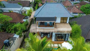 A two-story house with a thatched roof, a balcony with seating, and a large window. - Como Villa by Betterplace (Ubud)