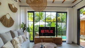A modern living room with a sofa, a coffee table, and a TV displaying 'NETFLIX'. - Como Villa by Betterplace (Ubud)