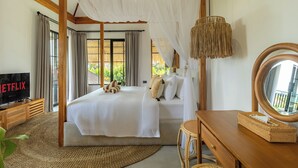 A bedroom with a canopy bed, a television, a wooden dresser, and a large mirror. - Como Villa by Betterplace (Ubud)