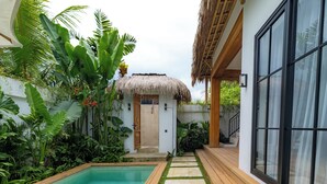 A pool area with a thatched-roof structure, surrounded by lush tropical plants.